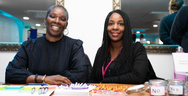 two female staff members sitting behind a desk full of stationary