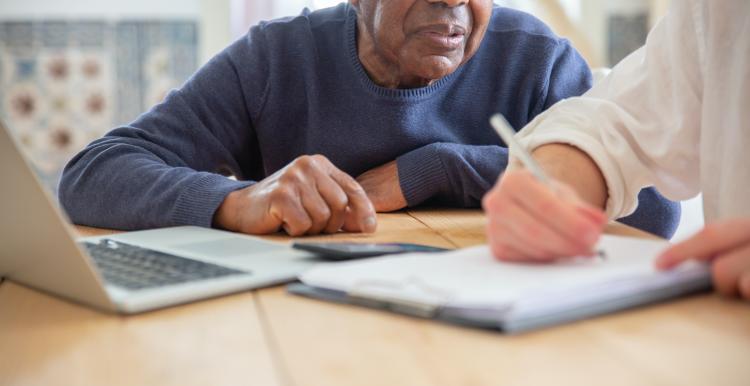 elderly man sat a laptop with a younger man transcribing his comments