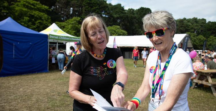 Two people discuss a document in the setting of a Pride festival in a field.