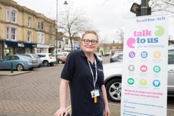 Female volunteer standing in front of a Healthwatch banner 