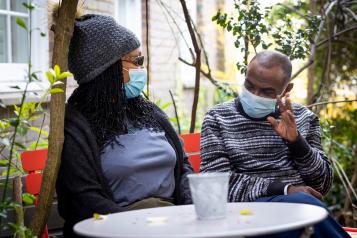 Man and woman sat outside chatting, wearing masks 