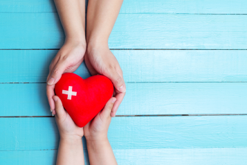 two sets of hands holding a cartoon heart, against a blue background