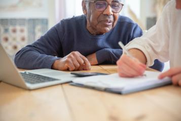 elderly man sat a laptop with a younger man transcribing his comments 