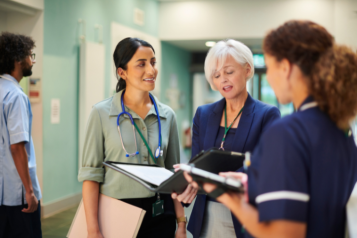 A group of three NHS staff members who are interacting with each other. They are all women of different ethnicities.