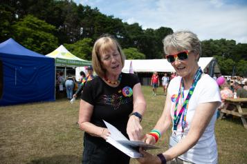 Two people discuss a document in the setting of a Pride festival in a field.