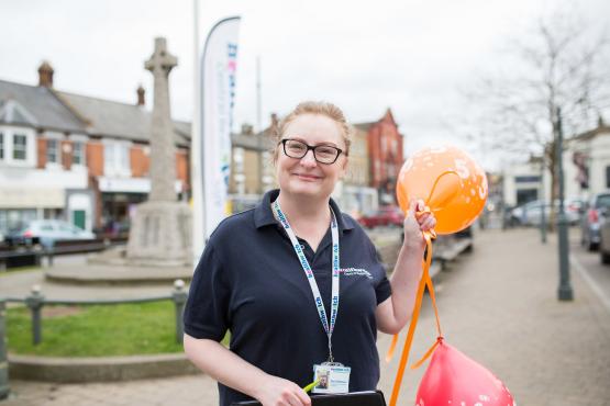Female volunteer standing in front of a Healthwatch flag holding two balloons