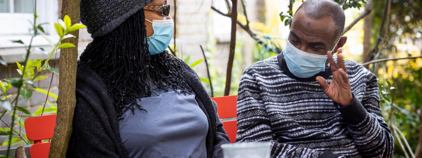 Man and woman sat outside chatting, wearing masks 